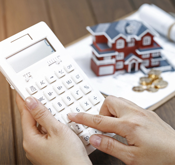 Persona calculando pagos para prestamos de casa junto a una maqueta de casa y unas llaves.