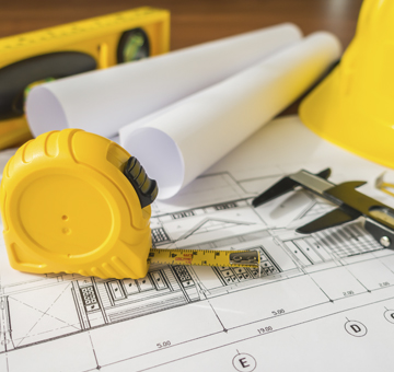 Planos de remodelación con cinta métrica y casco de obra.